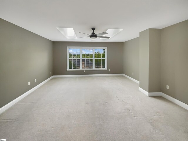 spare room with a skylight, baseboards, light colored carpet, and ceiling fan