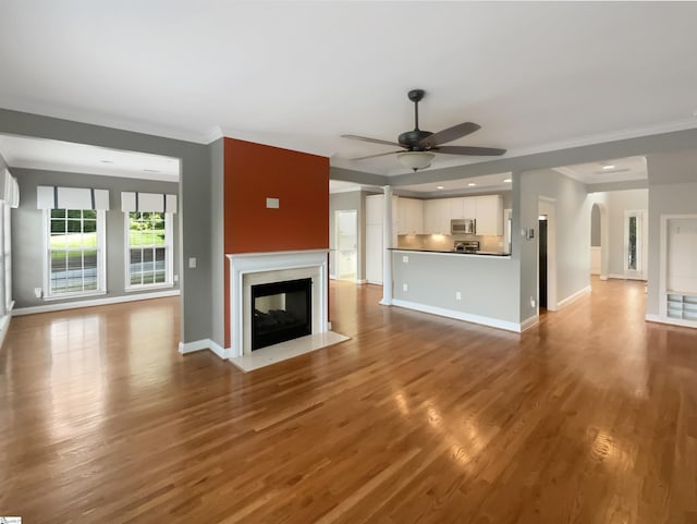 unfurnished living room featuring a ceiling fan, baseboards, wood finished floors, ornamental molding, and recessed lighting