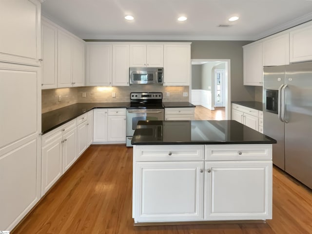 kitchen featuring appliances with stainless steel finishes, dark countertops, crown molding, white cabinetry, and light wood-style flooring