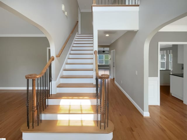 stairs featuring arched walkways, wood finished floors, crown molding, and baseboards