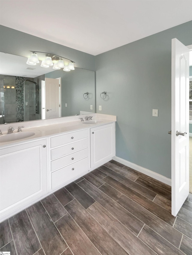 bathroom featuring wood finish floors, a shower stall, double vanity, and baseboards