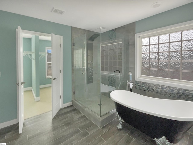 full bath featuring a stall shower, a freestanding bath, wood finished floors, a walk in closet, and decorative backsplash