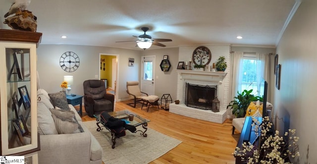 living area with crown molding, wood finished floors, healthy amount of natural light, a brick fireplace, and a ceiling fan