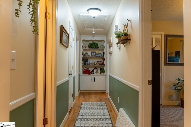 hallway with attic access, light wood-style flooring, and a textured ceiling