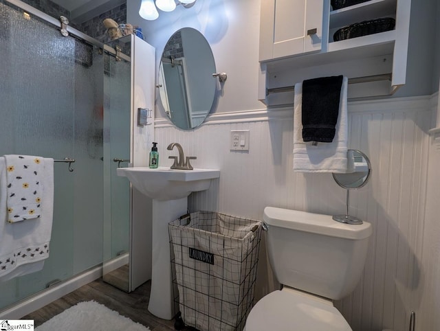 bathroom with a shower stall, wood finished floors, toilet, wainscoting, and a sink