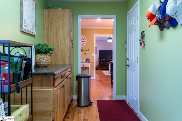 hallway featuring light wood-type flooring, crown molding, and baseboards