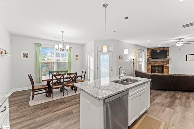 kitchen featuring a sink, dishwasher, a brick fireplace, light wood finished floors, and plenty of natural light