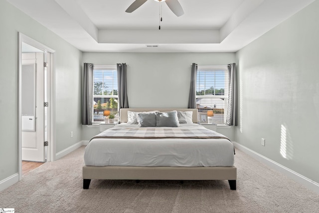 carpeted bedroom featuring a tray ceiling, multiple windows, baseboards, and a ceiling fan