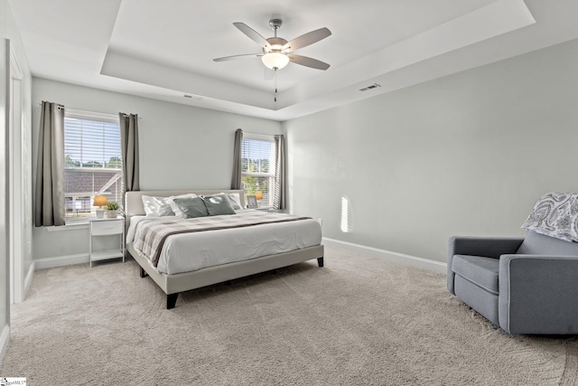 carpeted bedroom featuring a tray ceiling, baseboards, and ceiling fan
