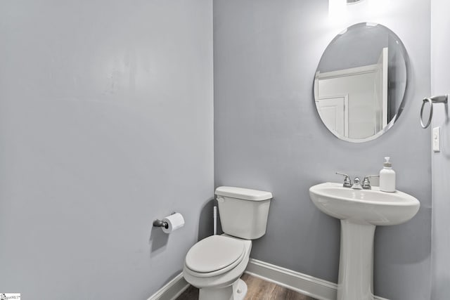 half bathroom with wood finished floors, toilet, baseboards, and a sink