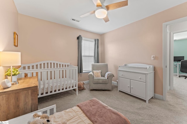 carpeted bedroom with a nursery area, ceiling fan, and baseboards