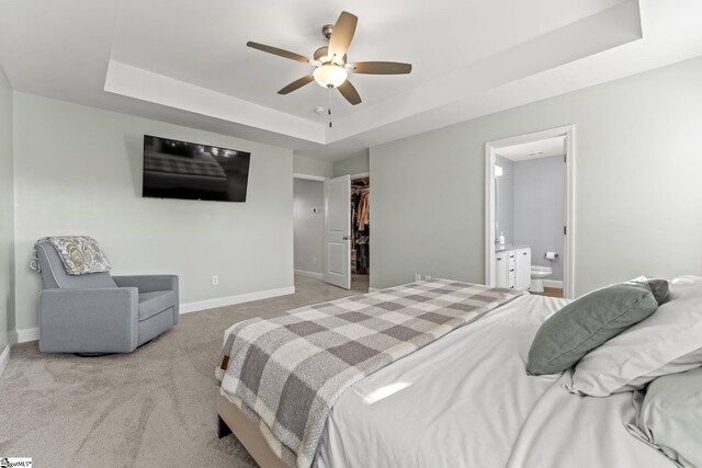 bedroom featuring a raised ceiling, baseboards, a walk in closet, and light colored carpet