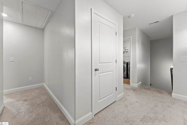 corridor with attic access, carpet flooring, baseboards, and washing machine and clothes dryer