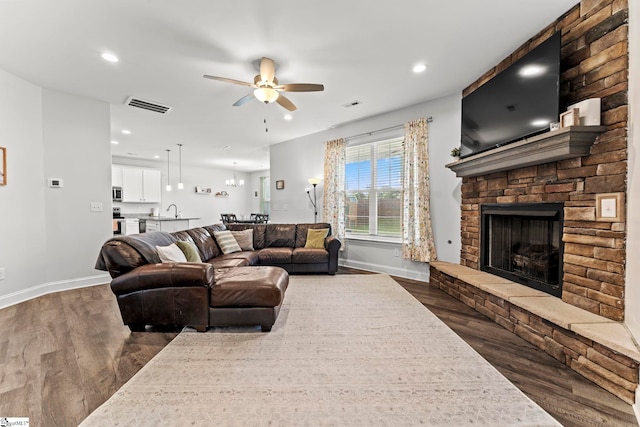 living area with dark wood-style flooring, baseboards, a ceiling fan, a stone fireplace, and recessed lighting
