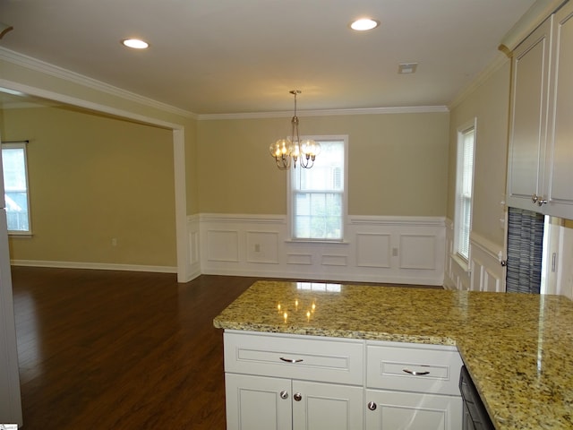 kitchen featuring dark wood-type flooring, a chandelier, ornamental molding, a wainscoted wall, and light stone counters