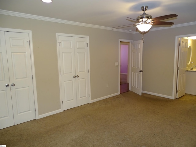 unfurnished bedroom with multiple closets, carpet flooring, crown molding, baseboards, and connected bathroom