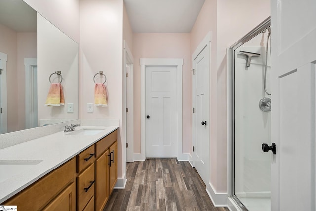 bathroom featuring a shower stall, wood finished floors, double vanity, and baseboards