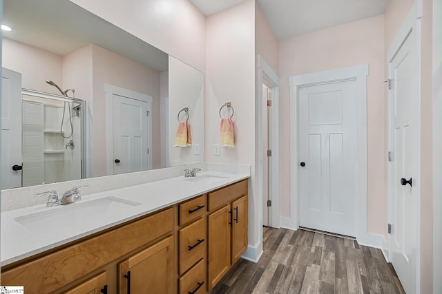 full bathroom featuring wood finished floors, double vanity, a shower stall, and baseboards