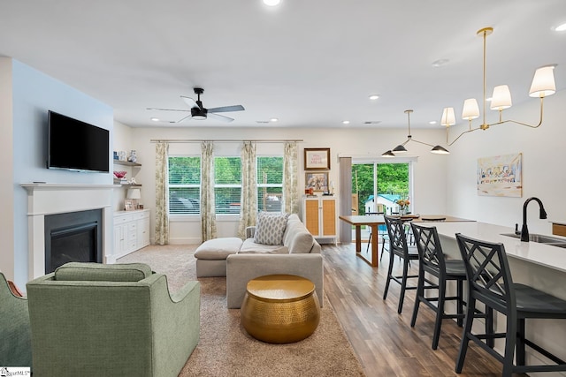 living room featuring ceiling fan, a glass covered fireplace, wood finished floors, and recessed lighting