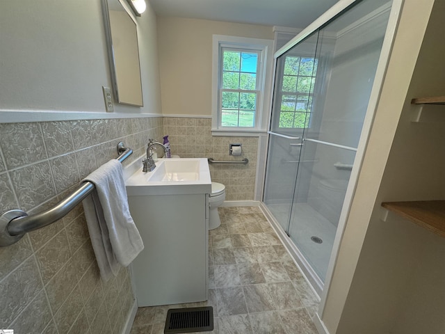 bathroom with toilet, a shower stall, tile walls, vanity, and a wainscoted wall