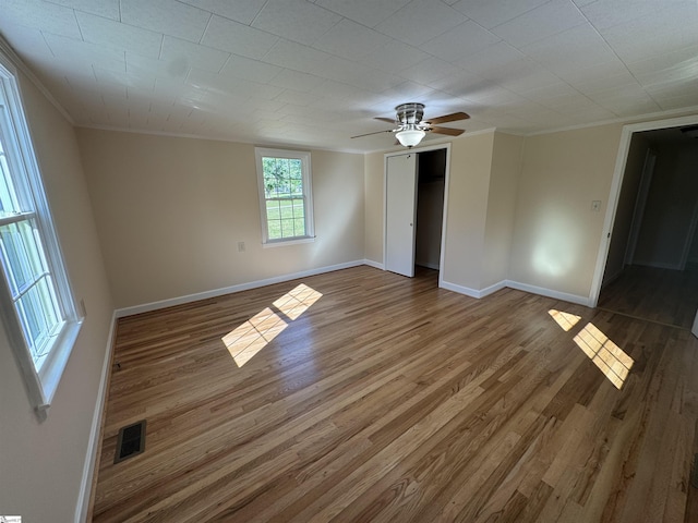 unfurnished bedroom featuring wood finished floors, baseboards, ornamental molding, a closet, and a ceiling fan