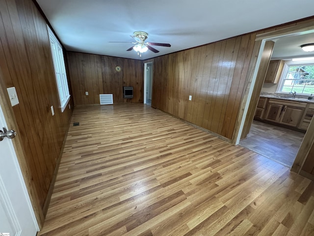 unfurnished room with a sink, a ceiling fan, light wood-style floors, heating unit, and wooden walls