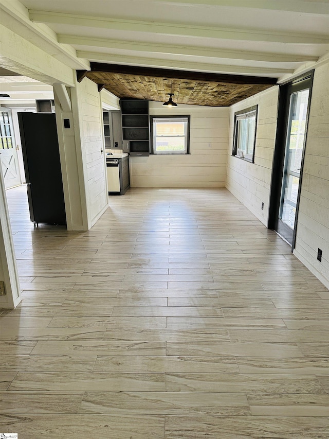 unfurnished living room with light wood finished floors, wood walls, beam ceiling, healthy amount of natural light, and a ceiling fan