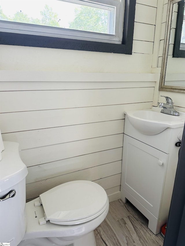 half bathroom featuring vanity, wooden walls, and toilet