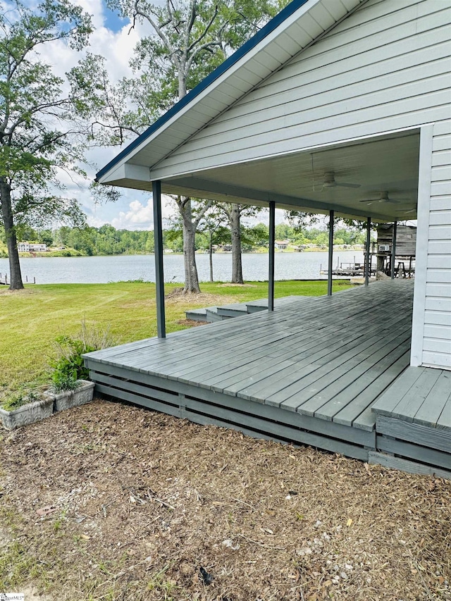 wooden deck with a water view, a lawn, and a ceiling fan