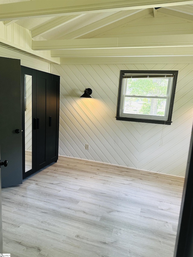 unfurnished room with beamed ceiling, light wood-style floors, and wood walls