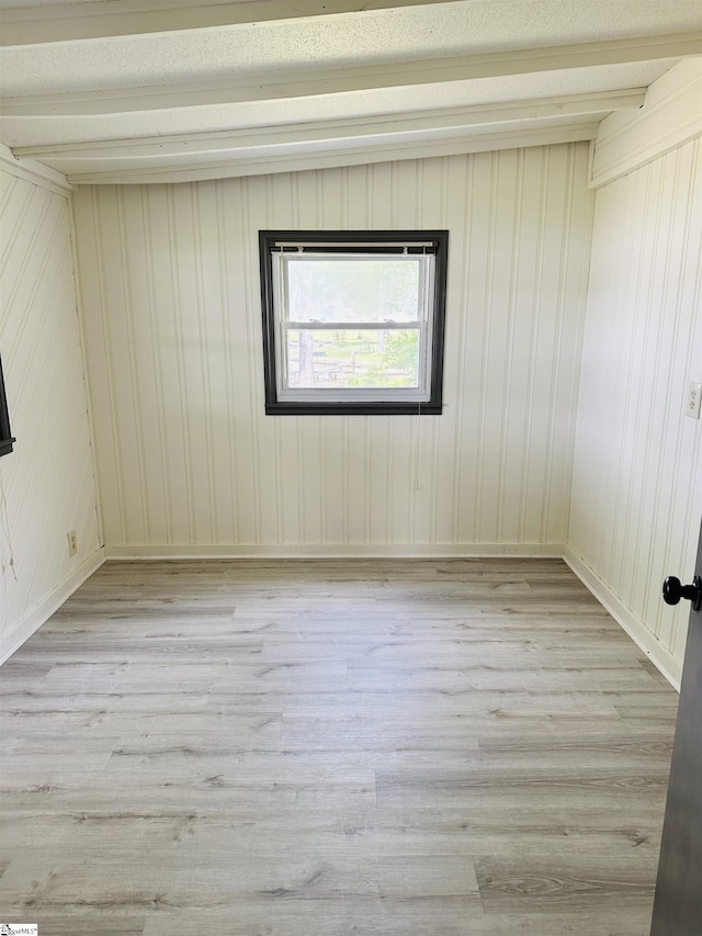 empty room with light wood finished floors, beam ceiling, and baseboards