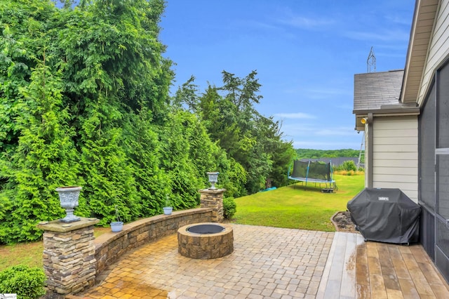 view of patio featuring a trampoline, a grill, and a fire pit