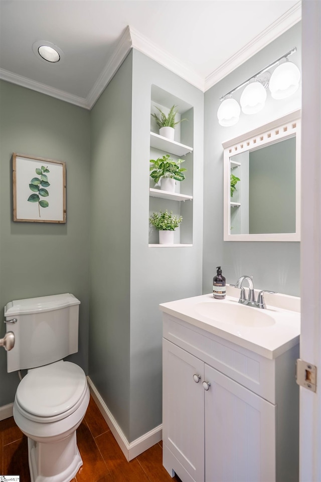 half bath with ornamental molding, vanity, wood finished floors, toilet, and baseboards
