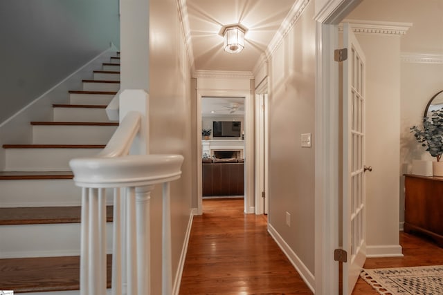 corridor with wood finished floors, stairway, ornamental molding, and baseboards