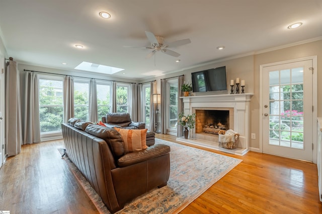 living area with a ceiling fan, a skylight, ornamental molding, a fireplace, and light wood-style floors