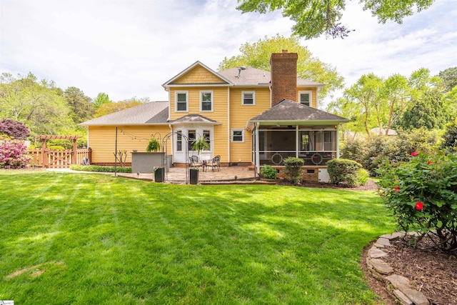 back of house with a chimney, a sunroom, a shingled roof, and a patio area