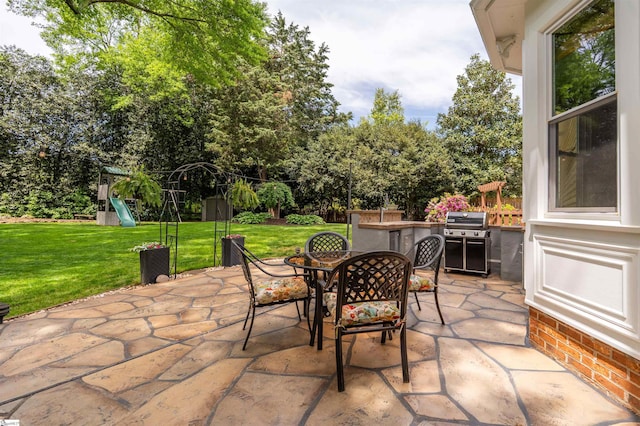 view of patio / terrace featuring outdoor dining space, a playground, area for grilling, and view of wooded area