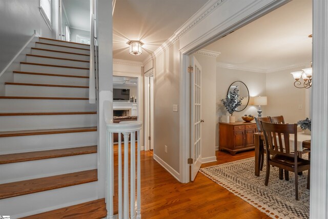 stairs with wood finished floors, a chandelier, baseboards, and crown molding