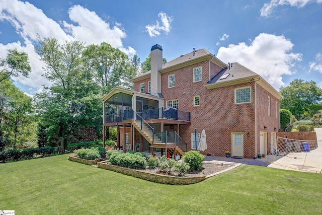 back of property with a sunroom, stairway, brick siding, a chimney, and a lawn