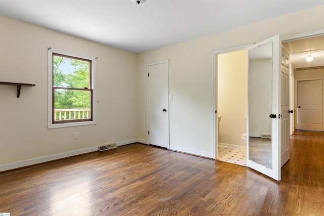 unfurnished bedroom featuring attic access, wood finished floors, baseboards, and ensuite bathroom