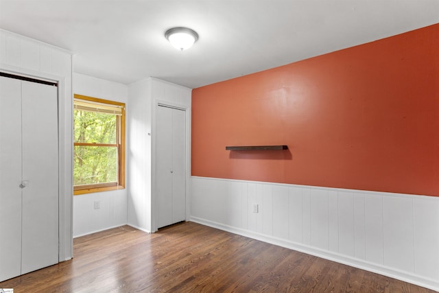 unfurnished bedroom featuring wood finished floors, a wainscoted wall, and multiple closets