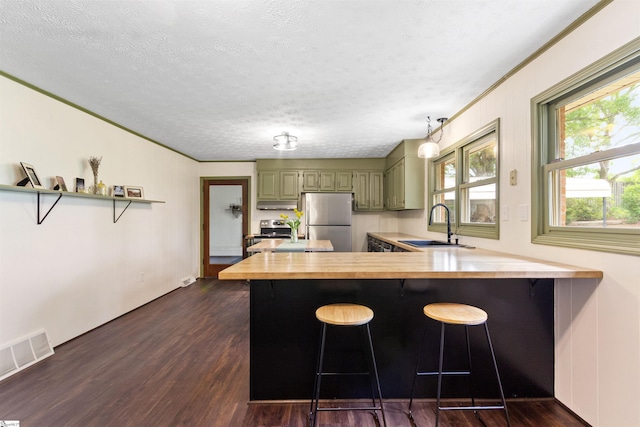 kitchen featuring freestanding refrigerator, butcher block counters, a sink, a peninsula, and green cabinets