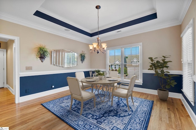 dining area featuring healthy amount of natural light, a raised ceiling, wood finished floors, and ornamental molding