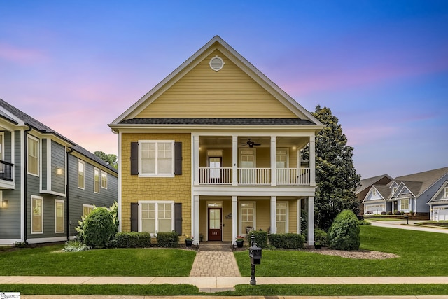 view of front of house featuring a balcony, a lawn, and a shingled roof
