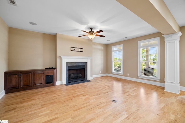 unfurnished living room featuring ornate columns, ceiling fan, light wood finished floors, a tiled fireplace, and baseboards