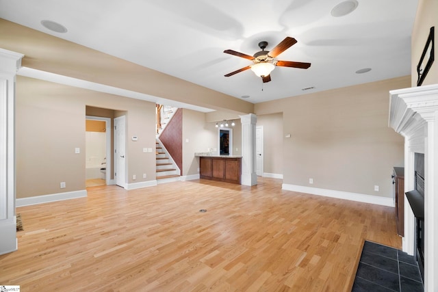 unfurnished living room with a fireplace with flush hearth, a ceiling fan, decorative columns, stairway, and light wood finished floors