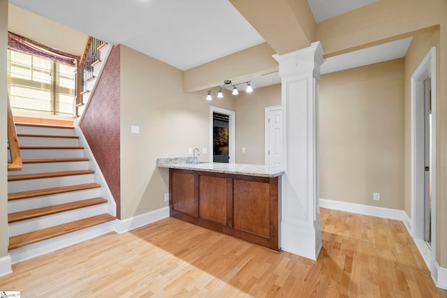 bar area with ornate columns, light wood-style floors, baseboards, stairs, and a sink