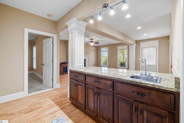 kitchen with a sink, a ceiling fan, light wood-type flooring, and light stone counters