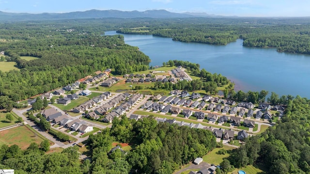 aerial view of property and surrounding area featuring a forest, a water and mountain view, and nearby suburban area