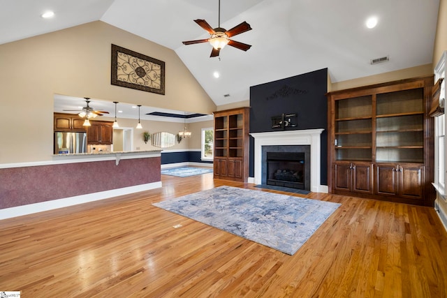 living area with ceiling fan, a fireplace with flush hearth, high vaulted ceiling, light wood finished floors, and a chandelier